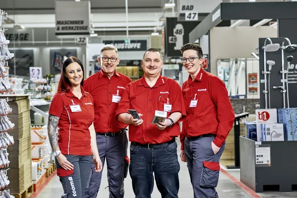 Vier lächelnde Personen in roter toom Arbeitskleidung in der Sanitär Abteilung.